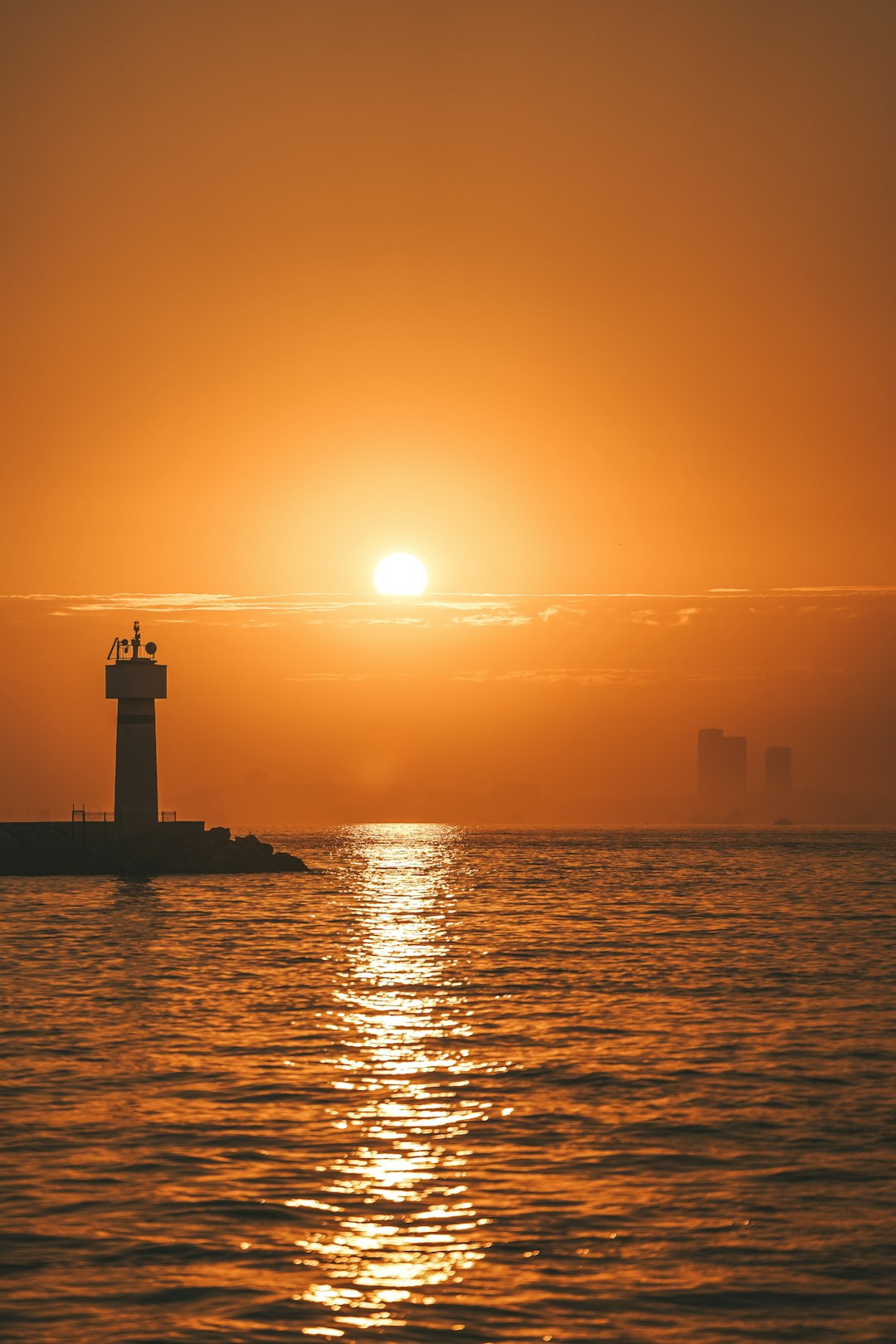 The sun is setting over the ocean with a lighthouse in the foreground